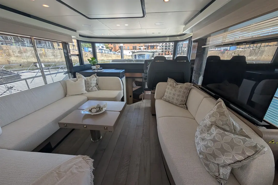 Luxury yacht interior featuring stylish seating, a coffee table with decorative items, and large windows overlooking the dock.